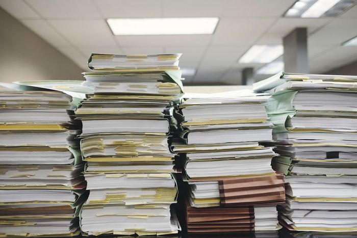 Stacks of paper documents and file folders waiting to be sorted