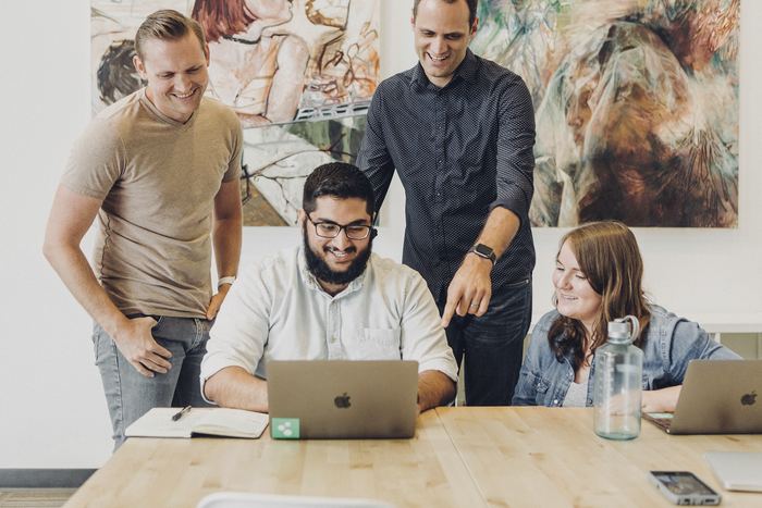 Four coworkers smiling around laptop at table
