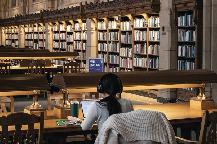 A student working at a desk in a warm, book-lined library